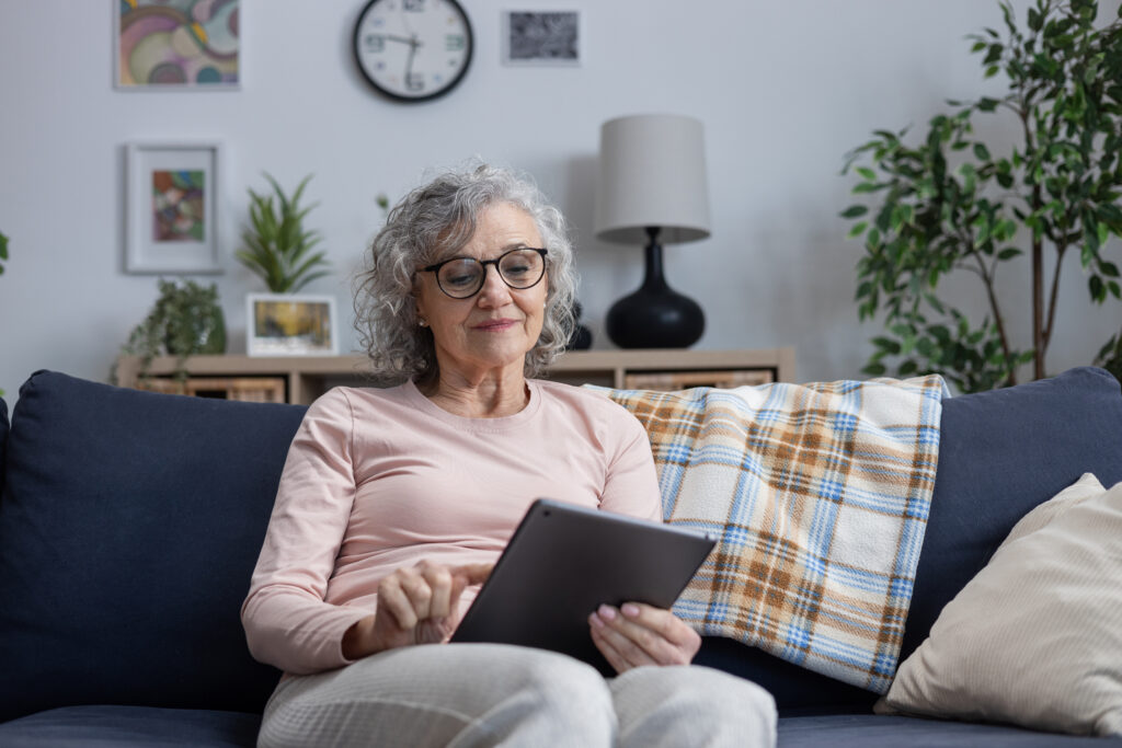 Senior woman sitting on sofa, smiling and touching a digital tablet screen at home